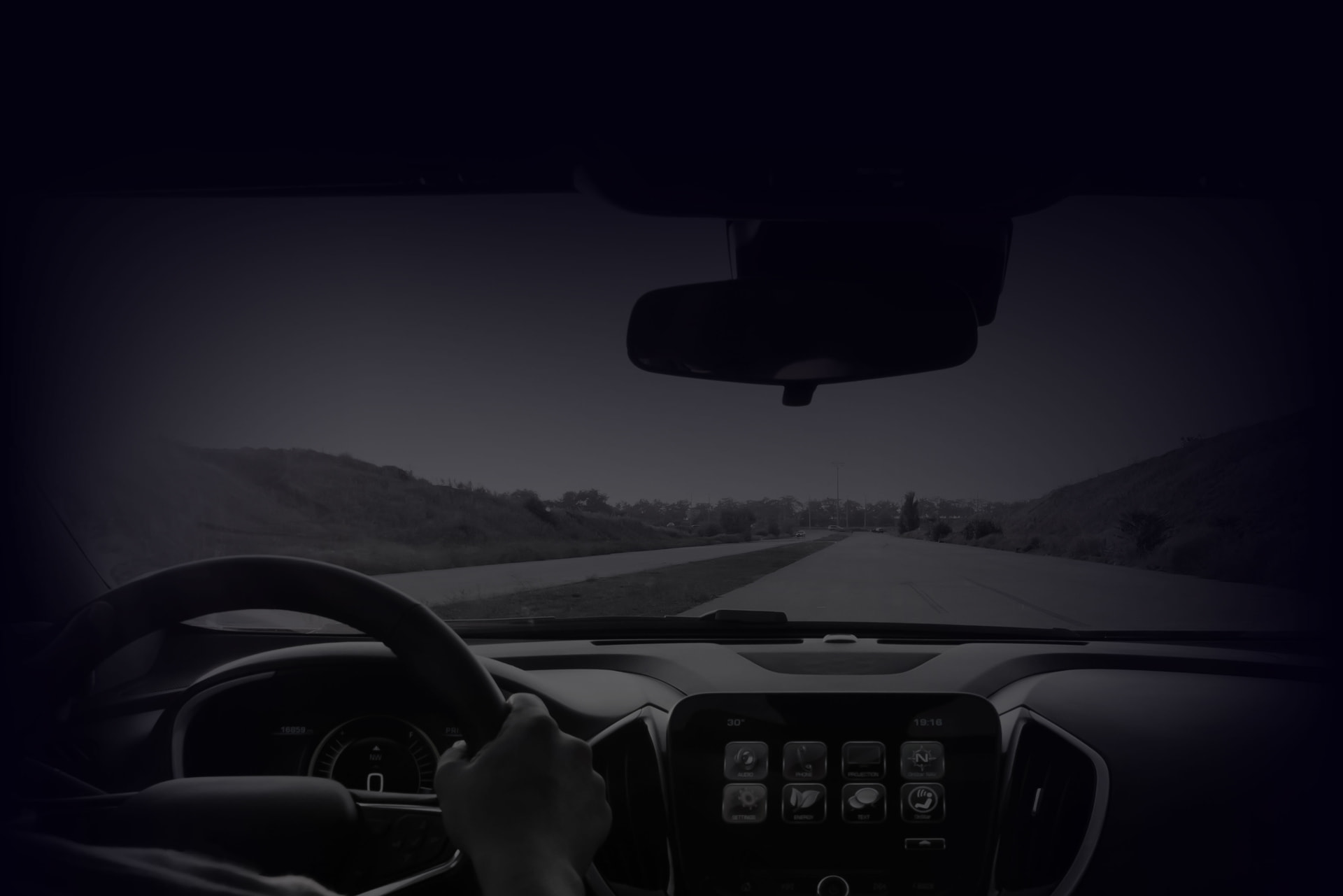 View through a car windscreen along an open road at dusk